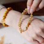 Wrist shot of a citrine crystal bracelet featuring a small gold gourd charm and polished crystal beads.